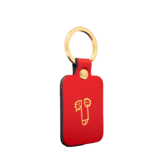 The Dick Key Ring - Red is a rectangular red leather keyring with a gold metal ring, featuring a simple yellow face line drawing on the front—a stylish piece of Estonian design for unique gift seekers. Set against a plain white background. Gate21.ee