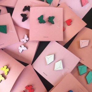 Kirju kõik kõrvarõngad earrings in geometric and butterfly shapes, available in various colours, are displayed on overlapping square pink cards—each card features a unique pair, highlighting Estonian design in the concept store display. Gate21.ee