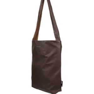 The Feel Good Bag - Chicory Coffee is a brown, rectangular Tinne+mia bag with a long strap, crafted from smooth leather-like material. Minimal detailing and a small black tag accent the lower right side. Gate21.ee