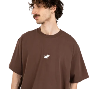 A person with wavy brown hair, a moustache, and an earring is wearing a loose black Moomin Heavy T-shirt featuring a small white animal graphic on the chest, posing against a plain white background. Gate21.ee