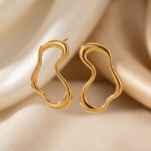 The Aversa - BØLD Earrings - Gold, featuring wavy open hoops with an abstract shape, are displayed on a cream-coloured satin fabric background. Gate21.ee