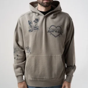 A person in a Westside Hoodie - Dark Sand, featuring black heart and cartoon graphics with "Run Up" text and stars, stands against a plain light background, channelling the playful style of RIPnDIP graphic T-shirts. Gate21.ee