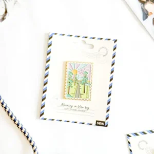 The Magnet – hommik Viru rabas is a pastel soft enamel magnet shaped like a postage stamp, showing a sunrise, trees, and path. It comes on a striped card labelled “Morning in View bay” and sits next to a New Rebels small rucksack and rope. Gate21.ee