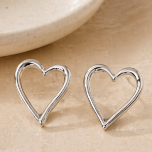 A pair of Nalani - BØLD Earrings - Silver rests on a beige surface beside the edge of a round ceramic dish. Gate21.ee