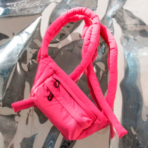 The Knotflex Pack - Red (Copy), featuring long tubular straps, a padded design, and a front zip pocket, is displayed on a reflective, crinkled metallic surface. Gate21.ee