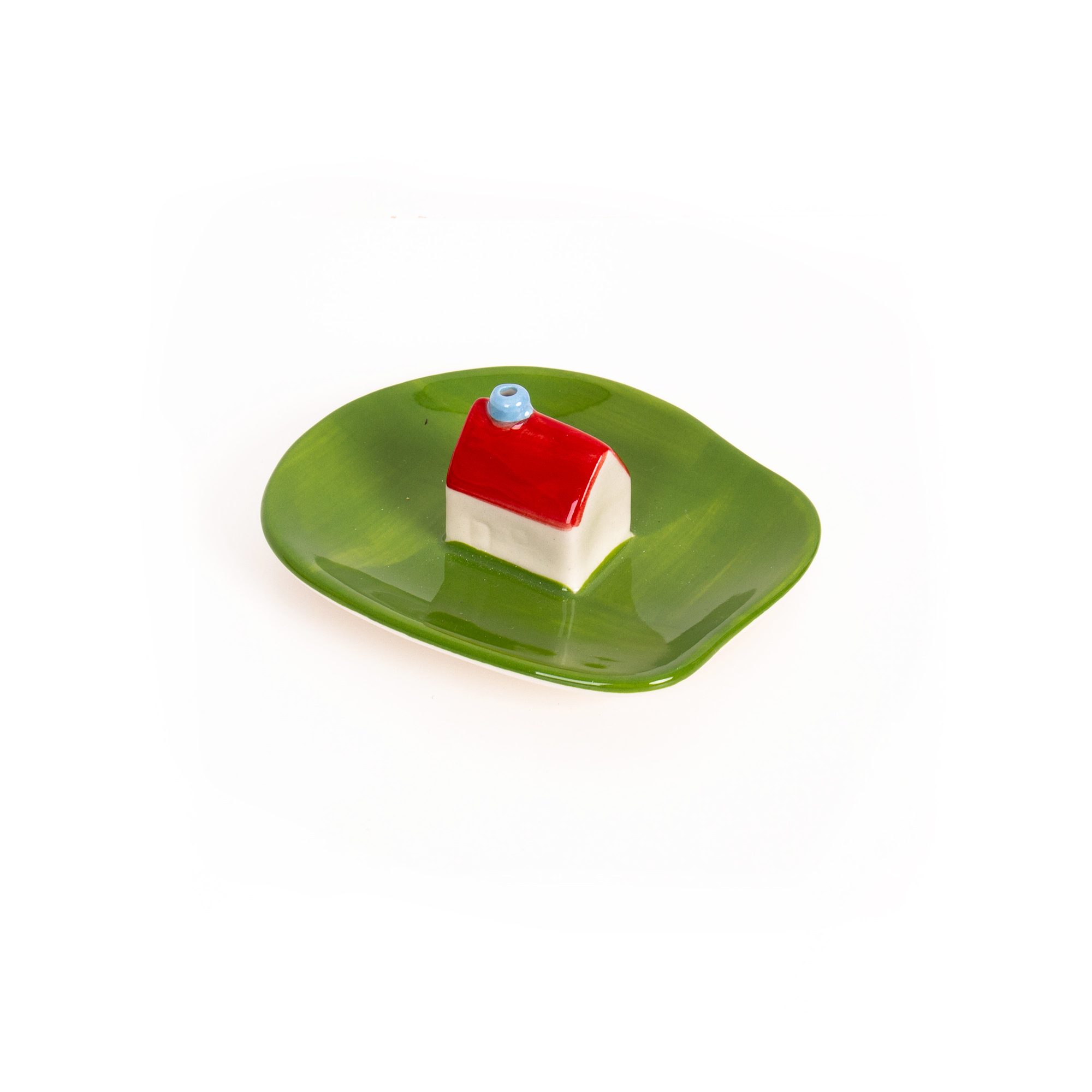 The Incense burner - Milk by Helio Ferreti features a small ceramic house with a red roof and blue chimney on a green, irregular plate, displayed against a white background. Gate21.ee