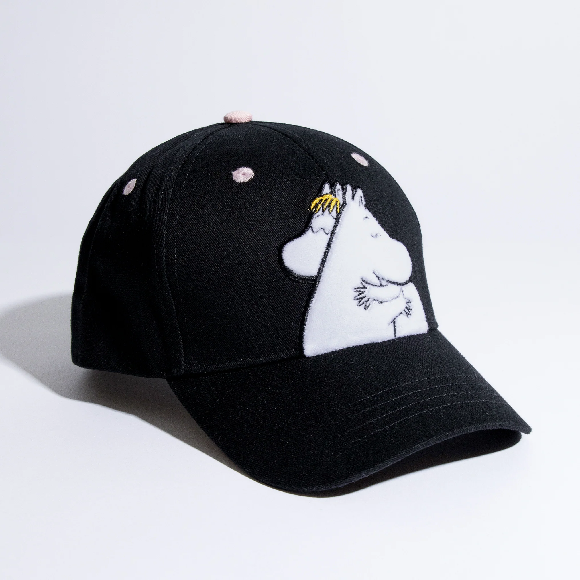 The Moomin Kids Cap is a black baseball hat featuring two white cartoon hippos hugging, pink spots on the crown, and embroidered details—perfect for fans of whimsical accessories and Moomin keyrings. Gate21.ee