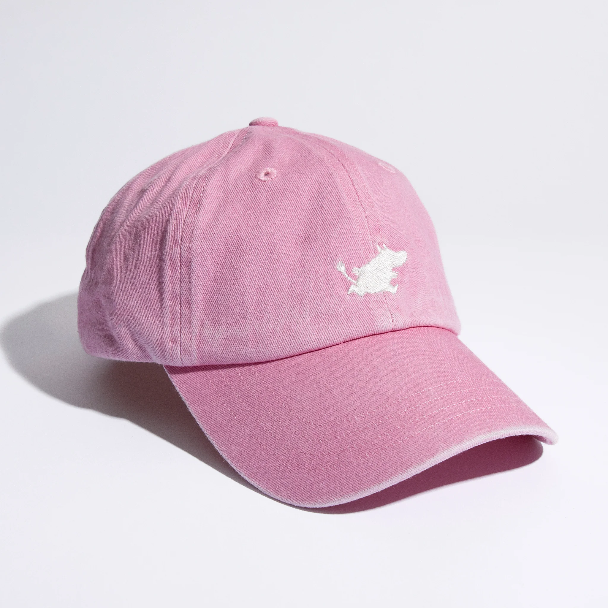 The Moomin Cap is a light pink baseball cap featuring a small white embroidered dog logo on the front, shown against a white background—ideal for pairing with your favourite Moomin keyrings. Gate21.ee