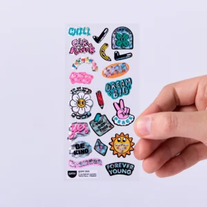 A hand holds a sheet of Donut - Fabulous Stickers, featuring playful illustrations, OMY sticker earrings, and phrases like CHILL, GIRL POWER, DREAM BIG, BE KIND. Gate21.ee