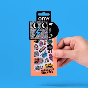 A hand holds a pack of Lashes - Fabulous Stickers (Copy), featuring a glittery square character, a black circle like a record, and colourful sticker earrings and pop icons on an orange background. Gate21.ee