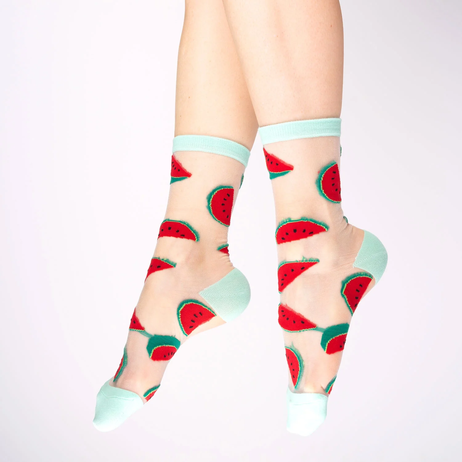 A pair of feet wearing Sunflowers - Transparent Socks, featuring light blue toe, heel, and cuff, decorated with playful sunflower patterns scattered across sheer fabric. The background is plain white. Gate21.ee