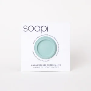 A round, yellow Soapi magnetic soap holder is shown in white packaging with the brand name and product details in English and German, highlighting that it’s made with about 90% recycled fishing nets. Gate21.ee