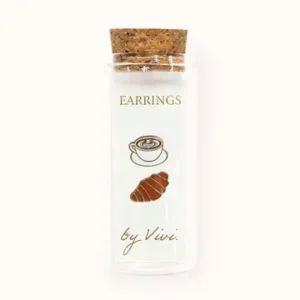 A clear glass phial with a cork stopper labelled "Tennis earrings by Vivi (Copy)," featuring illustrations of a coffee cup and a croissant on the front. Gate21.ee