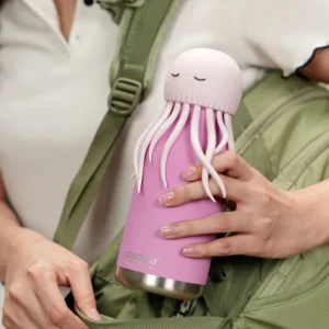 A person holds the Horse Bestie – 740ml, a pink ASOBU water bottle with a jellyfish-shaped lid featuring a rounded top and soft tentacles. Dressed in white and carrying a green rucksack, they highlight the bottle’s playful design. Gate21.ee
