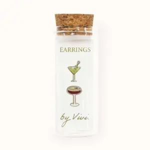 A clear glass phial with a cork lid holds two tennis earrings. The label reads "Tennis earrings by Vivi" and features images of a green martini and a brown cocktail glass. Gate21.ee