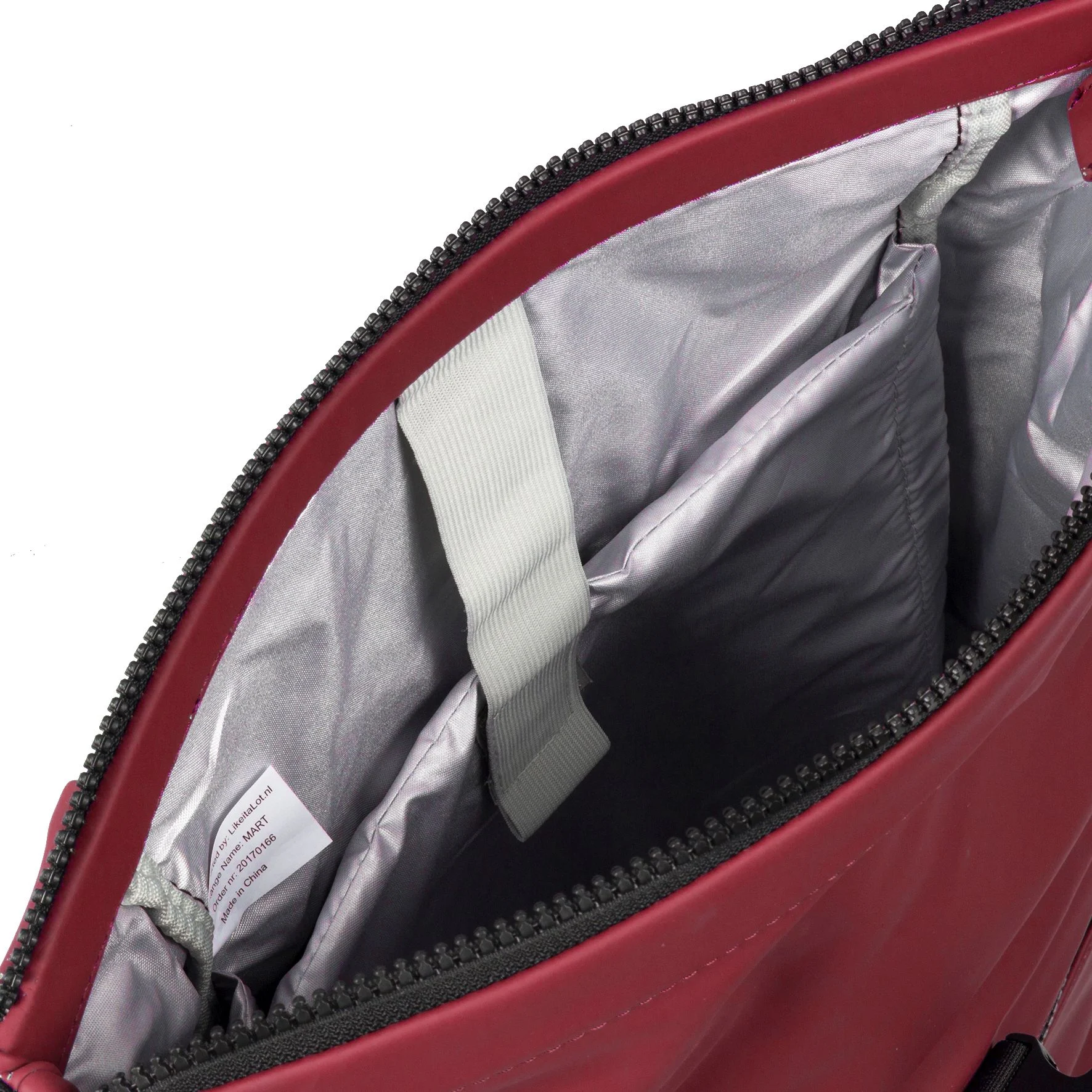 The image shows the inside of a burgundy New York Rolltop Rucksack by New Rebels, featuring a grey, padded lining and two compartments. A white tag with text and a grey fabric strap are visible near the opening, with a black zip partially visible along the edge. Gate21.ee