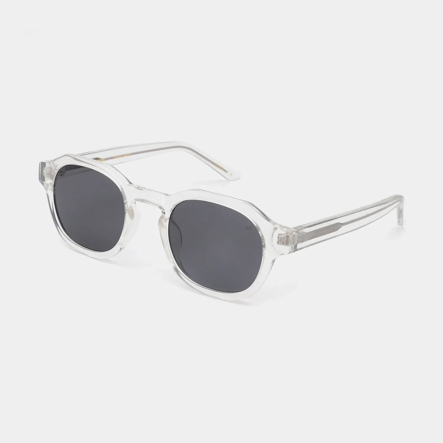 Clear-framed Zan - Blue Steel sunglasses by A. Kjærbede, featuring round dark lenses set against a plain white background. The slightly angular frames and transparent arms reveal metal detailing inside. Gate21.ee