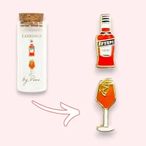 A small glass bottle labelled F*ck You earrings by Vivi is shown. Next to it are two enamel earrings: one shaped like a red liqueur bottle, the other like a wine glass with an orange drink and a slice of fruit—fun additions to Vivi’s playful collection, perfect for pairing with these bold F*ck You earrings. Gate21.ee