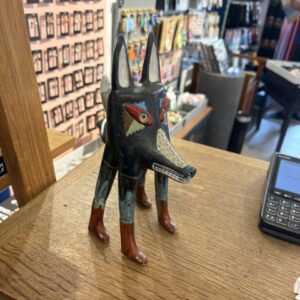 A painted wooden figurine, “Kauri hunt - suur,” with exaggerated wolf features and a sharp, legendary gaze stands on a wooden counter beside a payment terminal in a shop filled with diverse merchandise. Gate21.ee