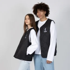 Two people stand side by side against a plain background, both wearing white Moomin T-shirts layered with the Snufkin Fishing Gilet Unisex in Black. They look calmly at the camera. Gate21.ee