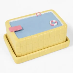 Introducing the Pool - Butter Dish: a rectangular ceramic butter dish crafted to resemble a swimming pool, featuring a yellow tiled exterior, blue lid, pink diving board, pink pool ladder, and a small life preserver detail—an ideal choice for fans of playful design or anyone looking for unique L’expressionist gifts. Gate21.ee