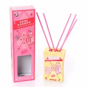 A yellow ceramic Happy Cat - 100ml Diffuser with pink sticks stands next to a pink box labelled Rose Garden. Both are adorned with playful designs, including playing cards and clover symbols, capturing the whimsical charm of Wick & Vessel home fragrance. Gate21.ee