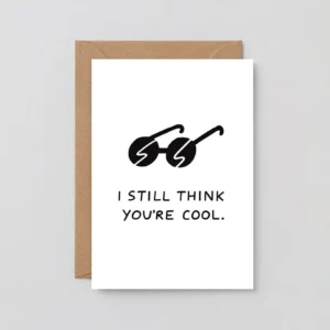The “Still Cool! - Greeting Card” features an illustration of black sunglasses and the phrase “I still think you’re cool.” It is displayed on top of a brown envelope against a plain, light background. Gate21.ee
