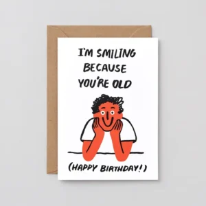 The You’re Old! - Greeting Card features a cartoon person smiling with text “I’M SMILING BECAUSE YOU’RE OLD” above and “(HAPPY BIRTHDAY!)” below. Comes with a brown envelope. Gate21.ee