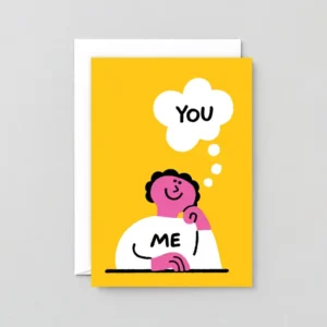 A cartoon with pink skin and black hair sits at a table in a white “ME” shirt, wrapping the Love You Dogs! - Greeting Card (Copy) as a thought bubble says “YOU” and a white envelope appears on the yellow background. Gate21.ee