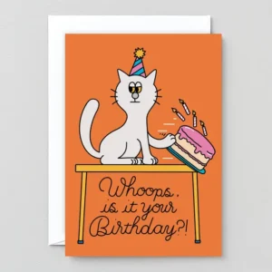 A cartoon cat in a party hat knocks over a birthday cake. The Whoops! - Greeting Card reads, “Whoops, is it your Birthday?!” Includes a partially visible white envelope behind the card. Gate21.ee