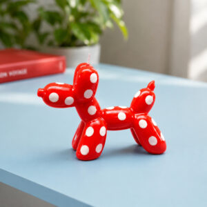 A red, Jeff Koons-style Balloon Dog Candle - Sunset (Copy) with white polka dots sitting on a blue surface. Gate21.ee